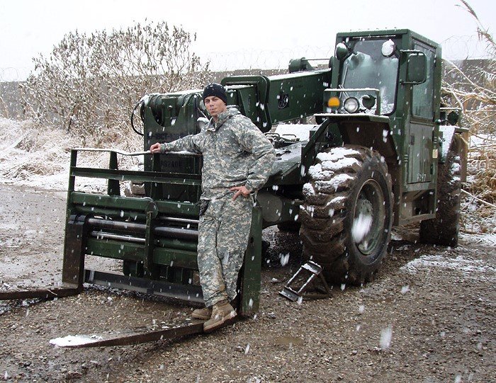 Daniel Kekipi leaning on large green military forklift during winter weather