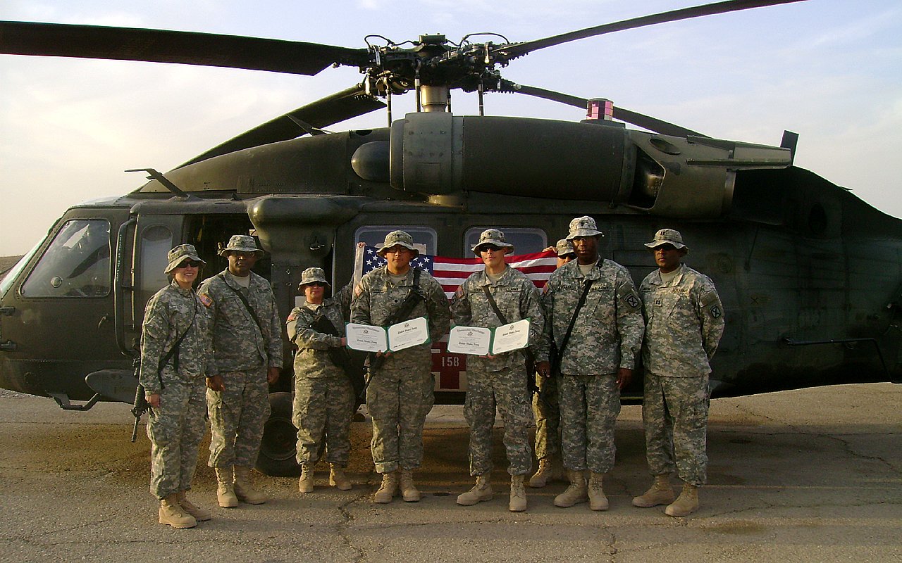 Group of soldiers posing with reenlistment certificates in front of Blackhawk helicopter