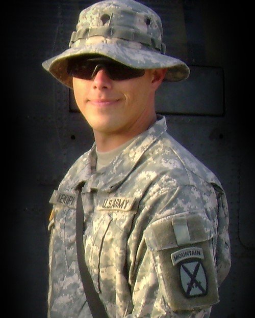 Daniel Kekipi in boonie hat and sunglasses standing in front of military helicopter