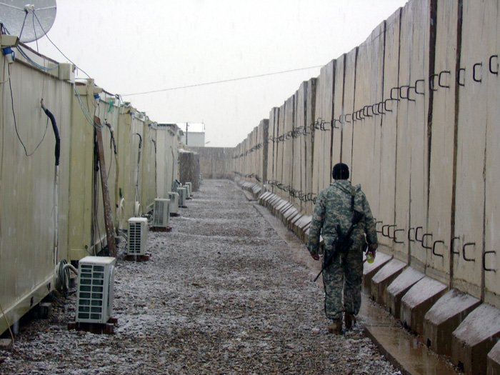 Soldier walking down gravel alley between concrete security barriers