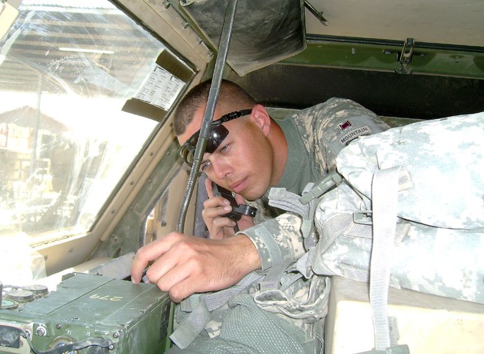 Daniel Kekipi holding radio handset and working on military communication unit inside vehicle